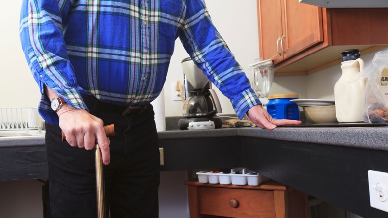 Man with Multiple Sclerosis standing in his accessible kitchen with a cane