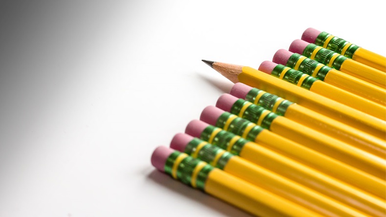 Row of pencil tops enter on an angle from bottom right with erasers flush and pointing toward center. Seventh pencil in stands out with sharpened lead tip jutting out further than adjacent erasers.