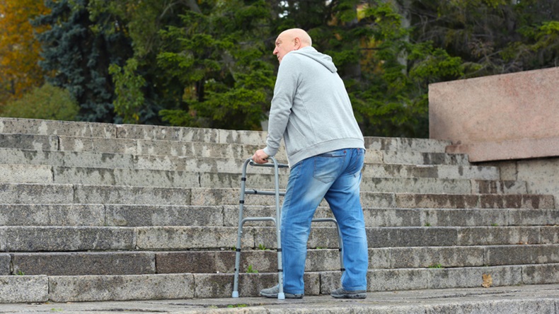 Elderly man with walking frame going up the stairs outdoors