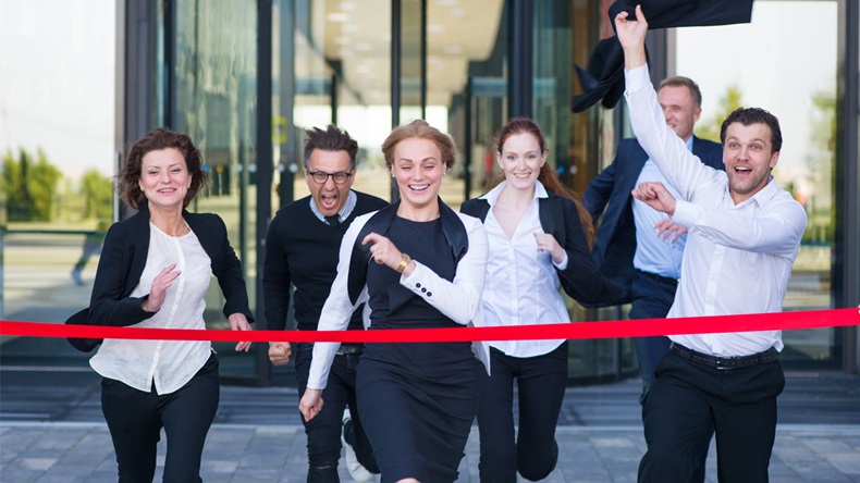Group of happy business people running from office building crossing red ribbon finish line