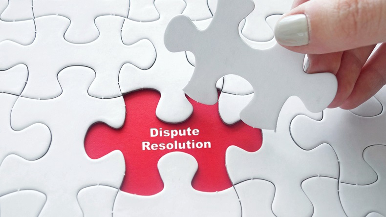 Close up of girl's hand placing the last jigsaw puzzle piece with word Dispute Resolution