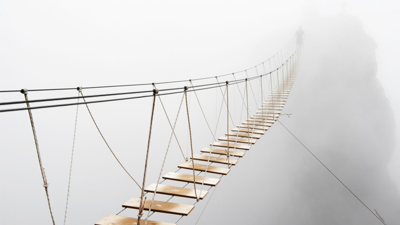Fuzzy man walking on hanging bridge vanishing in fog. Focus on middle of bridge. 