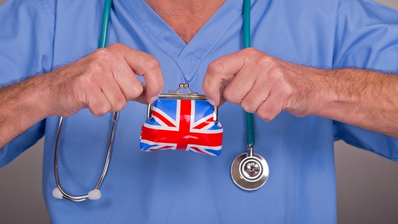 Male doctor/nurse wearing blue scrubs, with a stethoscope around his neck and holding a Union Jack money purse.