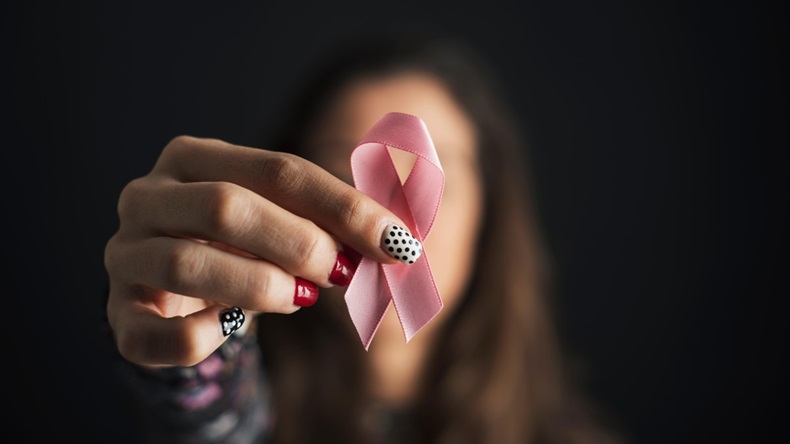 closeup of a young caucasian woman holding a pink ribbon in front of her face, for the breast cancer awareness 