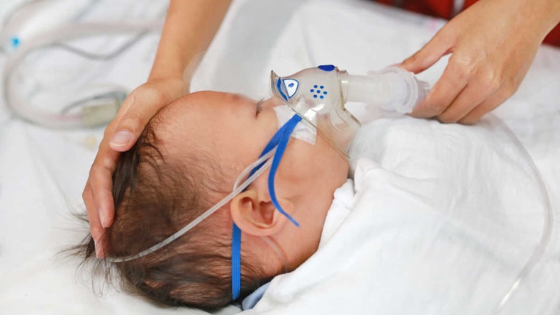 Toddler boy using nebulizer to cure asthma or pneumonia disease . Sick baby boy rest on patients bed and has inhalation therapy by the mask of inhaler. Respiratory Syncytial Virus (RSV).