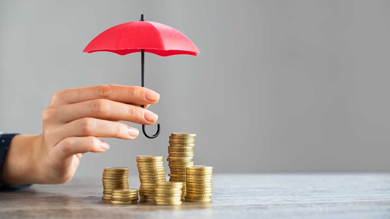 Young woman hand holding small red umbrella over pile of coins on table. Close up of stack of coins with female hands holding umbrella for protection. Financial safety and investment concept.