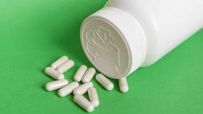White pills on green background and plastic bottle with blank label and copy space. Childproof packaging. Child resistant pill container. Push down and turn cap.