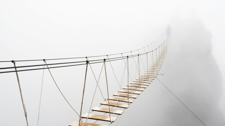 Fuzzy man walking on hanging bridge vanishing in fog. Focus on middle of bridge.