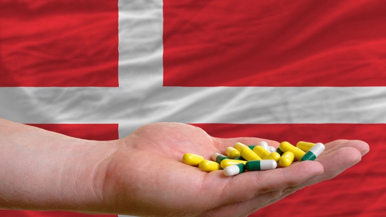 man holding capsules in front of complete wavy national flag of denmark symbolizing health, medicine, cure, vitamines and healthy life