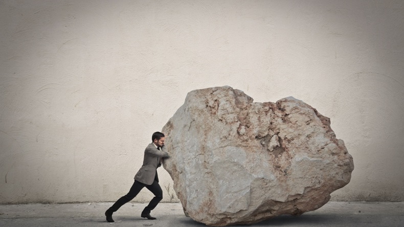man in suit pushing big boulder 