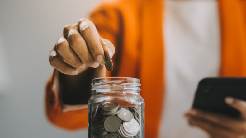 close up of person putting coins into a full jar of coins