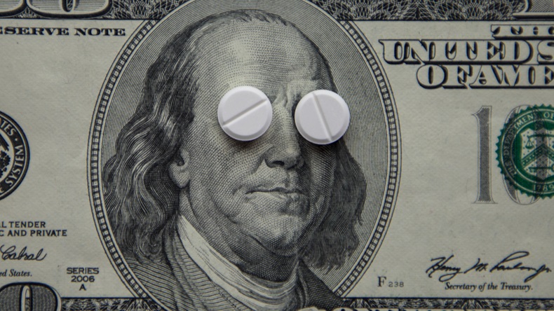 White round tablets lie in front of President Franklin, who is depicted on a hundred-dollar bill. The concept of the high cost of medicine, pharmaceuticals. - Image 