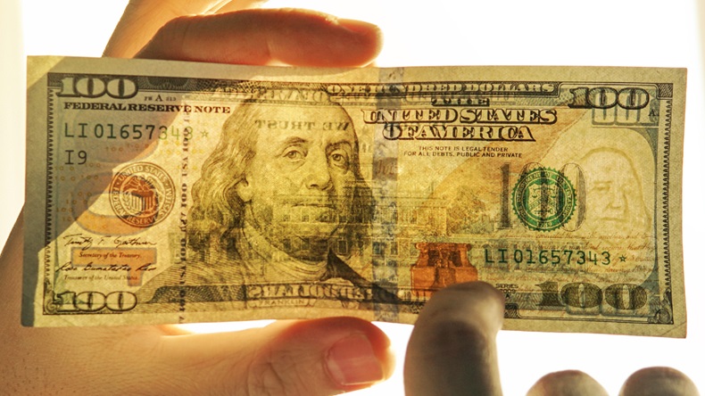Checking counterfeit money light. 100 dollars against the window in his hand. Check for watermark on new hundred dollar bill. translucence of the American currency. (source: shutterstock)